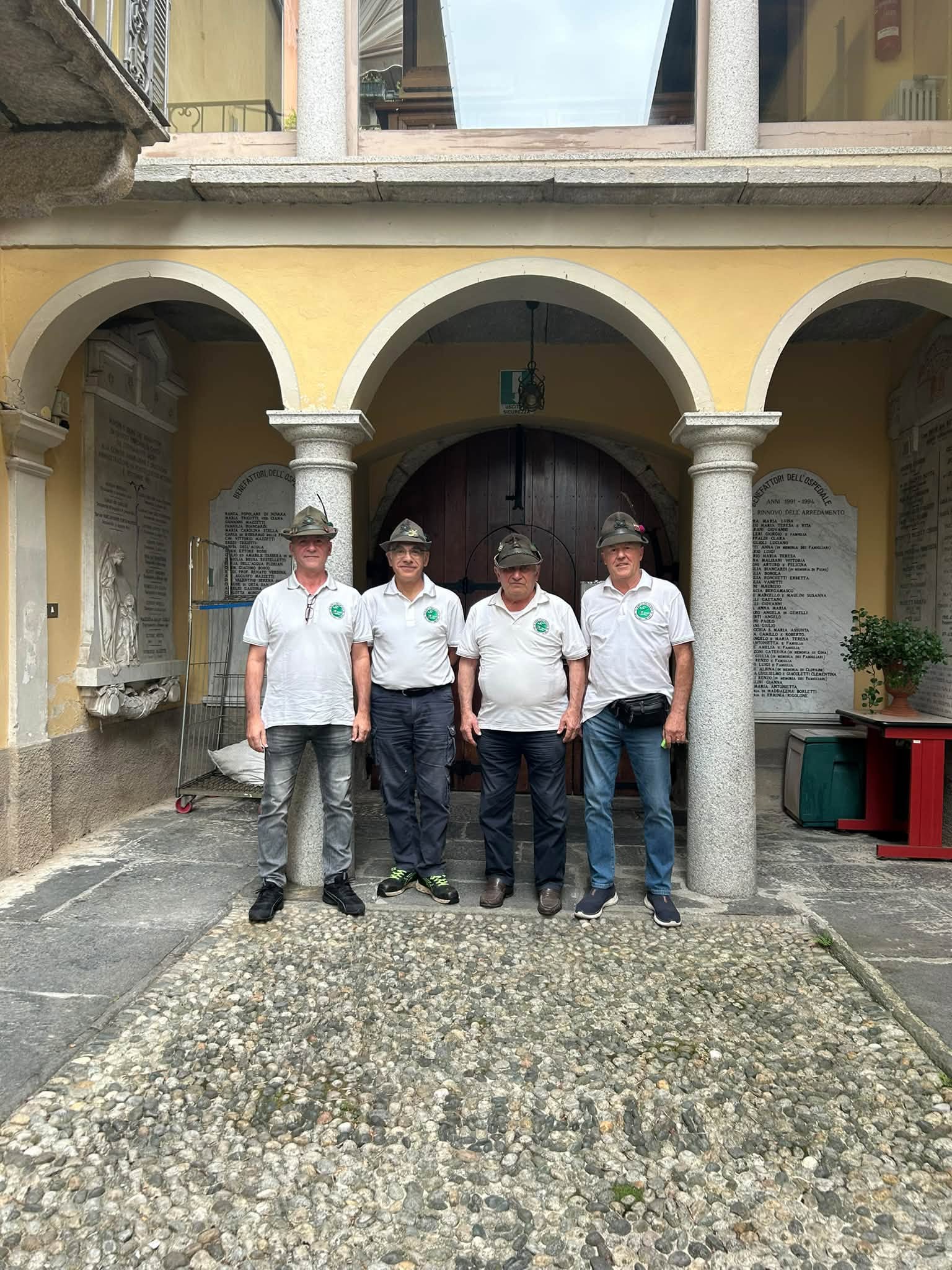 Quattro alpini con il cappello, in posa sotto il portico della corte